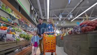 有小女儿的年轻父母在一家大型超市里选择新鲜水果。 商场超市销售，购物